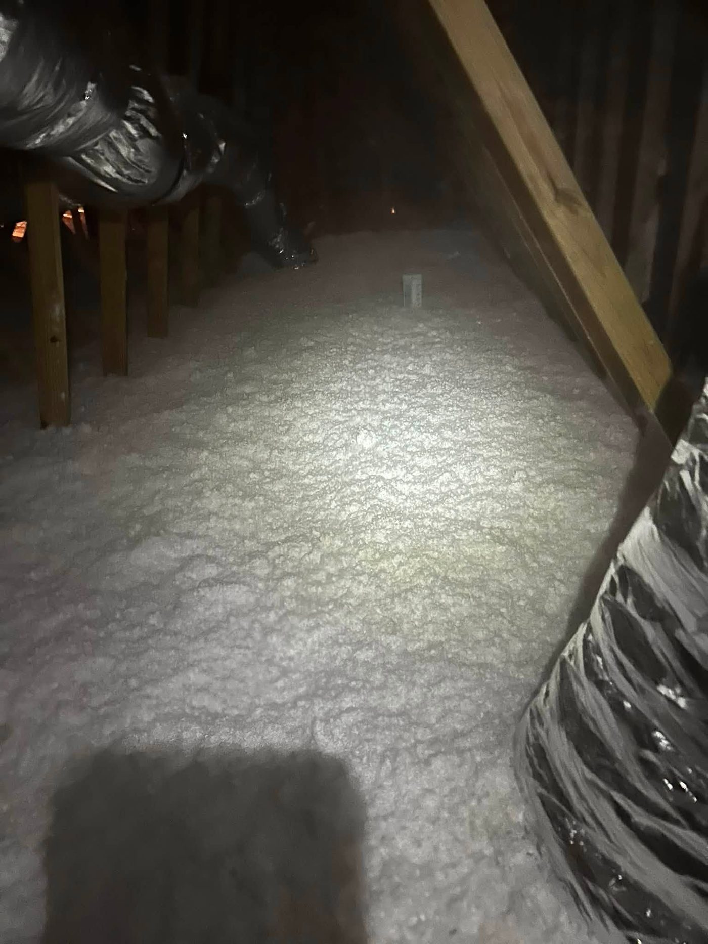 Fresh blown-in insulation installed evenly around flexible AC ducts in an attic