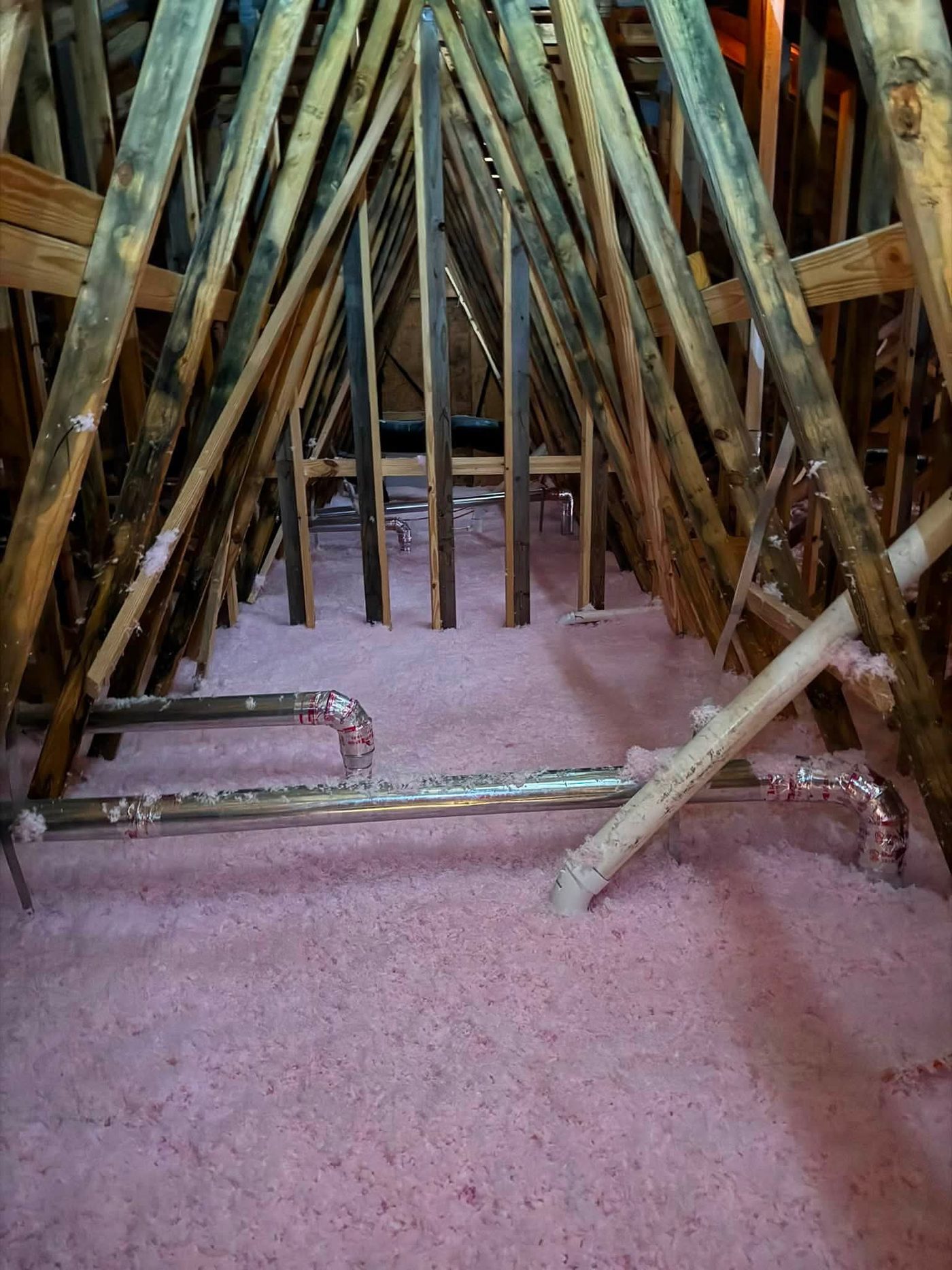 Fresh pink blown-in fiberglass insulation across an attic floor around plumbing lines